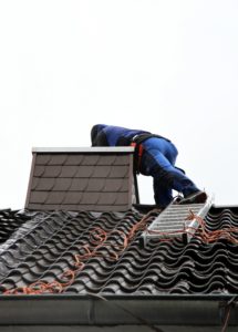 A technician standing on a roof and examining a chimney. His head and upper body are almost inside of the chimney.