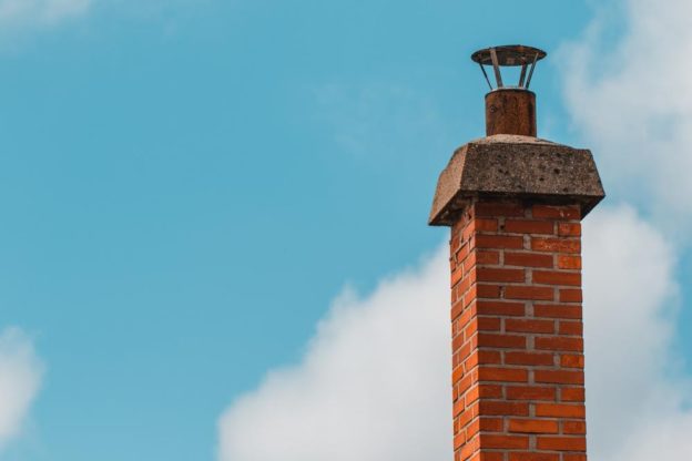 A brick chimney with a blue sky and clouds behind it.