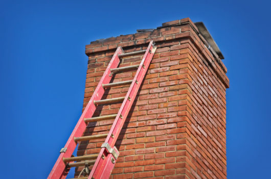a red ladder leaning against a red-brick chimney