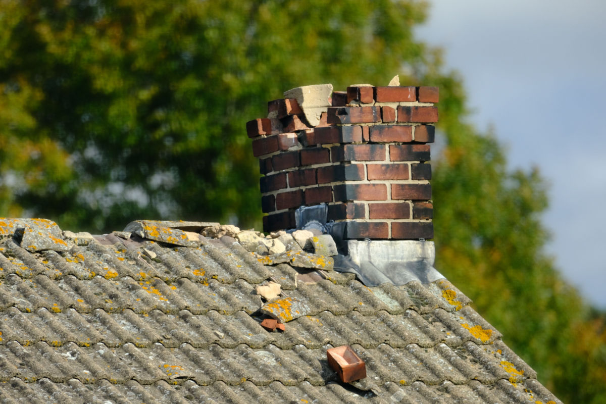 A crumbling brick chimney on the roof of a house.